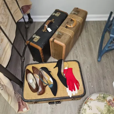 Sale Photo Thumbnail #23: Collection of vintage hard-shell suitcases, paired with women's dress shoes and gloves, arranged on a light wood-look floor.