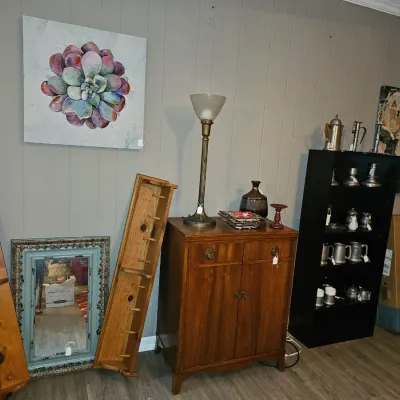 Sale Photo Thumbnail #52: Collection of home furnishings including a traditional wooden cabinet, a tall brass floor lamp, wooden wall pegs, wall art, and a black bookshelf filled with pewter tankards.
