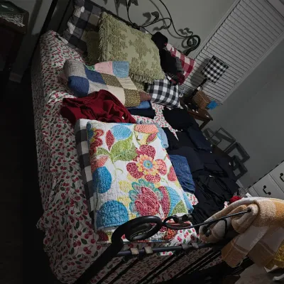 Sale Photo Thumbnail #20: Black wrought iron bed frame with scrollwork details, featuring a collection of colorful quilts, decorative pillows, and linens.