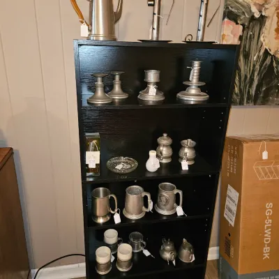 Sale Photo Thumbnail #2: Black wooden bookshelf displayed with a collection of pewter tableware, including coffee pots, candlesticks, and drinking mugs.