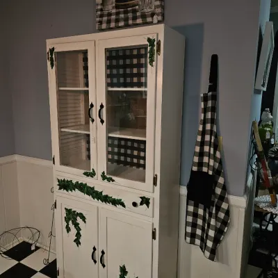 Sale Photo Thumbnail #67: White hand-painted hutch featuring ivy detailing, glass display doors, and a black and white buffalo plaid interior lining.