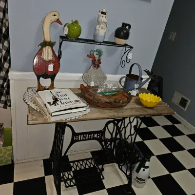 Sale Photo Thumbnail #63: Vintage Singer treadle sewing machine base repurposed as a console table with rustic wooden top, featuring various country-style home decor items and figurines.