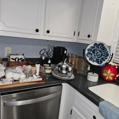Sale Photo Thumbnail #39: Assortment of kitchen decor and toiletries, including a decorative blue ceramic plate on a stand, a red floral pitcher, and a tray of soaps.