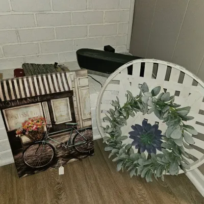 Sale Photo Thumbnail #8: French bakery themed printed canvas wall art alongside a round whitewashed tobacco basket with a faux greenery wreath.