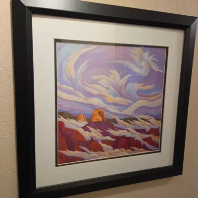 Sale Photo Thumbnail #306: Framed Southwestern landscape print depicting desert rock formations under dramatic swirling clouds, presented in a black composite frame with double matting.