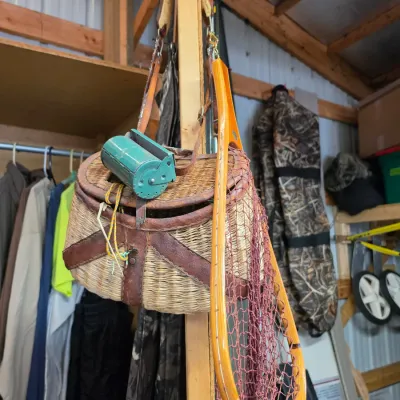 Sale Photo Thumbnail #76: Vintage wicker fishing creel with leather harness, green tackle box accessory, and a wooden landing net with mesh netting.