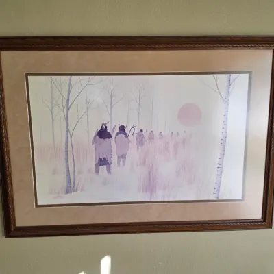 Sale Photo Thumbnail #263: Framed Native American art print by Bev Doolittle depicting figures walking through a snowy landscape, presented in a carved wooden frame with double matting.