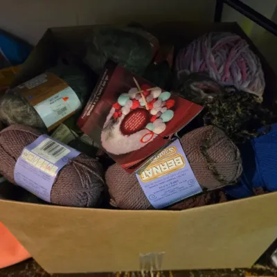Sale Photo Thumbnail #163: Cardboard box filled with various skeins of knitting and crochet yarn, including Bernat Softee Chunky brands.