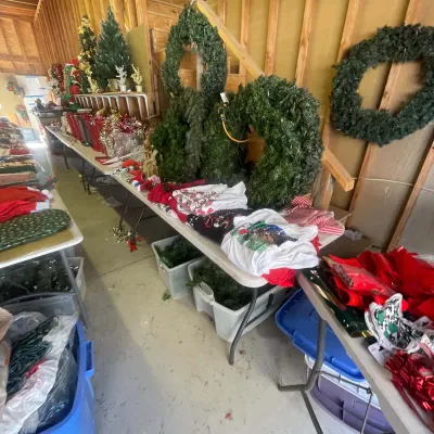 Sale Photo Thumbnail #129: Collection of Christmas decorations including artificial wreaths, mini trees, festive linens, and storage totes arranged on folding tables.