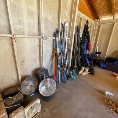Sale Photo Thumbnail #114: Assortment of winter sports gear and small appliances, including K2 and Kästle skis, ski boots, space heaters, and portable fans stored in a shed.