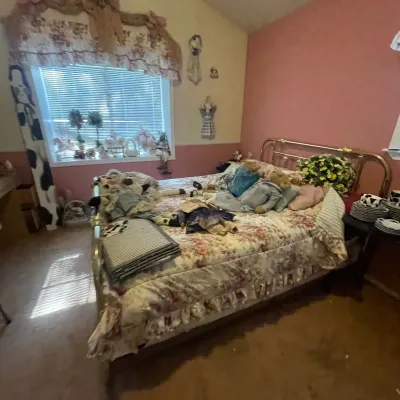 Sale Photo Thumbnail #72: Traditional brass bed frame with a floral pattern bedspread, decorative pillows, stuffed bears, and vintage-style dolls in a pink bedroom.