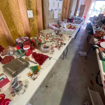 Sale Photo Thumbnail #138: Folding tables packed with various Christmas decorations, including ornaments, figurines, tins, and tinsel decorations.