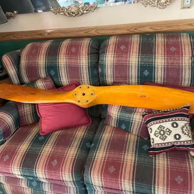 Sale Photo Thumbnail #43: Vintage wooden airplane propeller resting on a plaid upholstered loveseat, featuring a glossy varnish finish and original maker decals.