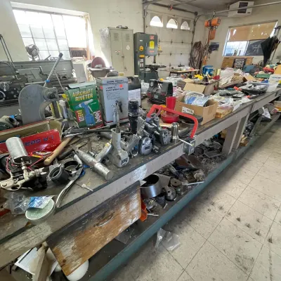 Sale Photo Thumbnail #106: Workshop workbench filled with assorted pneumatic tools, paint spray guns, boxed equipment, and hardware.