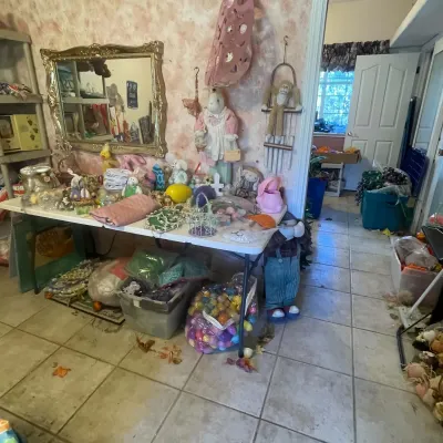 Sale Photo Thumbnail #116: A folding table displaying an assortment of Easter and spring decor, plush rabbits, plastic eggs, and hanging wall items beneath an ornate gold-framed mirror.