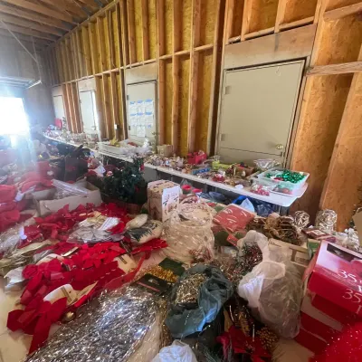 Sale Photo Thumbnail #125: Large assortment of holiday decorations and Christmas ornaments arranged on tables inside an unfinished garage or workshop.