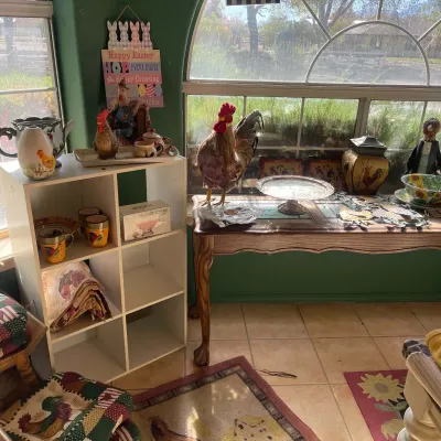 Sale Photo Thumbnail #47: Collection of farm-themed home decor, including rooster figurines, mug sets, glassware, and a white laminate cubby shelf unit alongside a wooden console table.