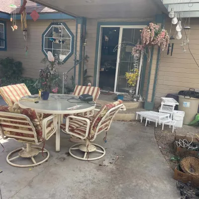 Sale Photo Thumbnail #86: Outdoor patio dining set featuring a round glass-top table and four metal swivel armchairs with striped floral cushions, alongside various yard decor and plastic side tables.