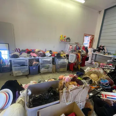 Sale Photo Thumbnail #143: Large collection of costume accessories, hats, props, and clothing items displayed on tables and racks in a storage area.