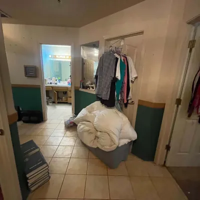 Sale Photo Thumbnail #70: Collection of household items for sale, including a stack of books, a plastic bin filled with comforters, and assorted clothing on a doorway rack.