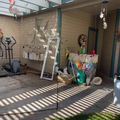 Sale Photo Thumbnail #83: Covered patio area featuring an elliptical machine, Tiki-style bar set up with grass skirting, decorative fishing nets, wind chimes, and various yard decorations.