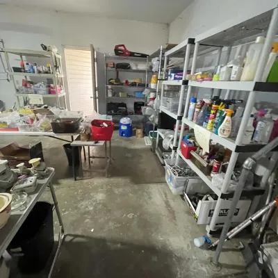 Sale Photo Thumbnail #26: Garage space setup filled with plastic and wire shelving units, folding tables, cleaning supplies, and various household items for sale.