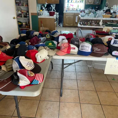 Sale Photo Thumbnail #52: Large collection of vintage baseball and trucker hats displayed on folding tables, including novelty, agricultural, and souvenir designs.