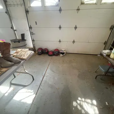 Sale Photo Thumbnail #20: A collection of motorcycle helmets lined up along a garage door, featuring four red full-face and half-helmets alongside one white dirt bike helmet, with cowboy boots visible nearby.