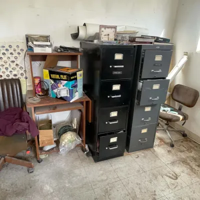 Sale Photo Thumbnail #45: Two tall metal filing cabinets standing alongside a wooden computer desk, vintage office chairs, and assorted storage items.