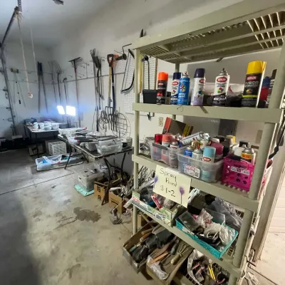 Sale Photo Thumbnail #23: Plastic shelving unit loaded with various spray paint cans priced at $1-2 each, situated in a garage with garden tools and worktables.