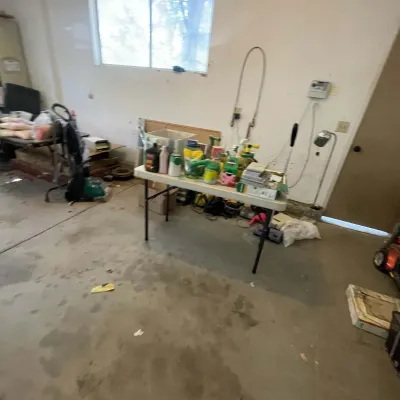 Sale Photo Thumbnail #22: A collection of lawn and garden supplies, automotive fluids, and household chemicals arranged on a white folding table in a garage.
