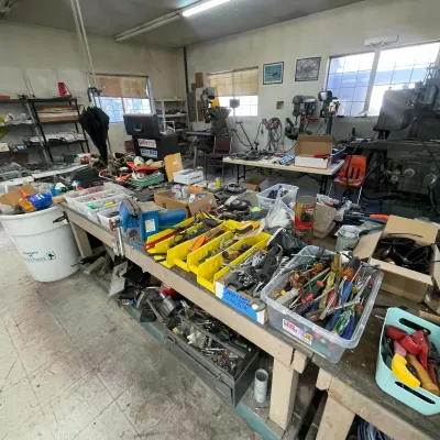 Sale Photo Thumbnail #92: Workshop workbench filled with various hand tools, hardware bins, bench vices, and machinery equipment.