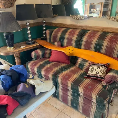 Sale Photo Thumbnail #49: Vintage Sensenich wooden airplane propeller displayed across a plaid upholstered sofa, flanked by table lamps and baseball caps.