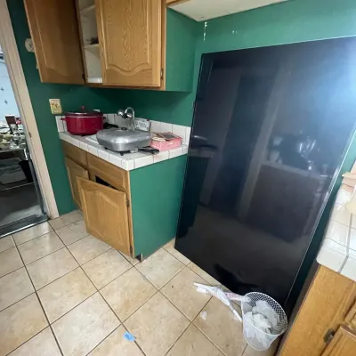 Sale Photo Thumbnail #14: Large black flat-screen television resting on the floor in a kitchen with green walls and oak cabinets.