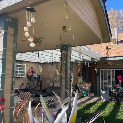 Sale Photo Thumbnail #84: Covered patio containing an assortment of outdoor decor, wind chimes, solar lights, patio chairs, and exercise equipment.