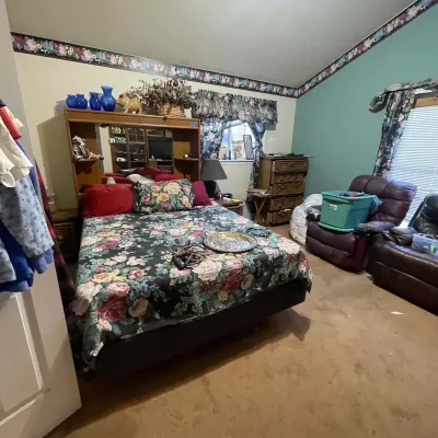 Sale Photo Thumbnail #6: Bedroom set including a queen bed with a dark floral comforter, a wood headboard with a mirrored back, a matching tall dresser, and recliner armchairs.