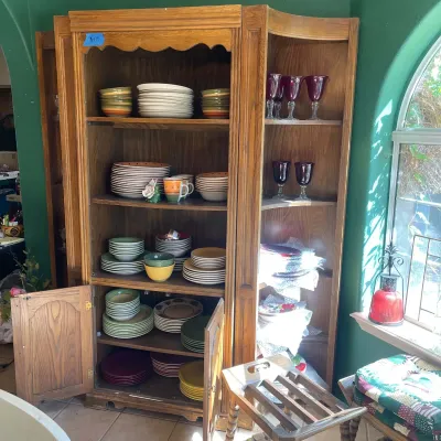 Sale Photo Thumbnail #53: Large wooden corner china hutch filled with colorful ceramic tableware, stemware, and serving dishes.