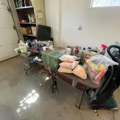 Sale Photo Thumbnail #27: Folding workbench filled with garage items, including a green power supply unit, cleaning supplies, packaged materials, and an upright vacuum cleaner.