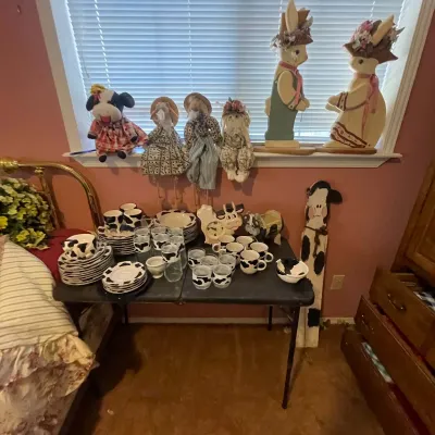 Sale Photo Thumbnail #71: Collection of country farm-themed decor, featuring cow-print ceramic dishes and glassware alongside wooden rabbit figurines and fabric dolls.