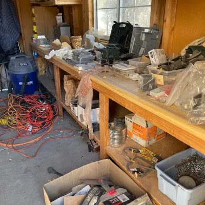 Sale Photo Thumbnail #89: Workshop area featuring wooden workbenches cluttered with various tools, hardware, extension cords, a Shop-Vac wet/dry vacuum, and storage bins.