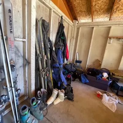 Sale Photo Thumbnail #113: Collection of vintage ski gear stored in a shed, including Kastle and Rossignol skis, ski boots, and padded travel bags.