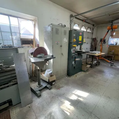 Sale Photo Thumbnail #93: Workshop loaded with industrial machinery, featuring a standing disc sander, metal storage locker, vertical band saw, and engine hoist.