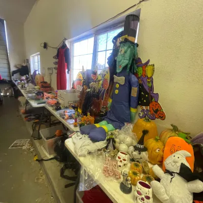 Sale Photo Thumbnail #146: Collection of Halloween decorations including plush figures, decorative pumpkins, skull ornaments, and paper cutouts displayed on tables.