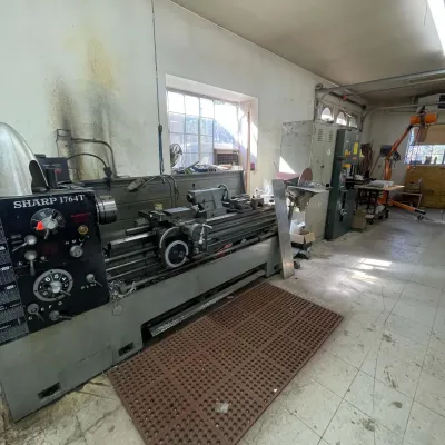 Sale Photo Thumbnail #87: Sharp 1764T heavy-duty precision engine lathe situated in a workshop setting, complete with control knobs and metalworking attachments.