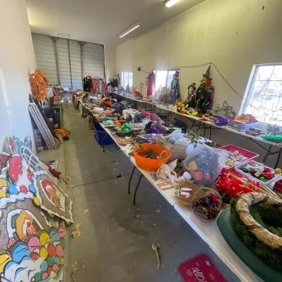Sale Photo Thumbnail #135: Large collection of seasonal holiday decor displayed on tables in a garage, featuring Halloween witch figures, costumes, and Christmas ornaments.