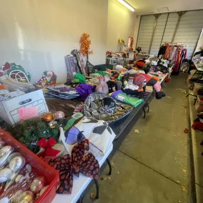 Sale Photo Thumbnail #148: Large collection of seasonal decorations, costumes, hats, and holiday ornaments displayed on long folding tables in a garage.