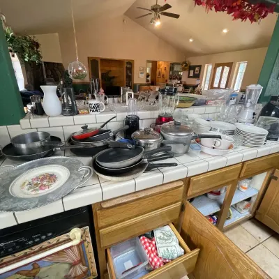Sale Photo Thumbnail #15: Collection of assorted kitchenware, including stainless steel pots and pans, small countertop appliances, mugs, glassware, and tableware arranged on a tiled kitchen island.