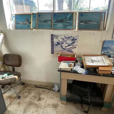 Sale Photo Thumbnail #46: Collection of framed vintage airplane prints lined up on a windowsill above a Hughes Air Force poster and a workshop table.