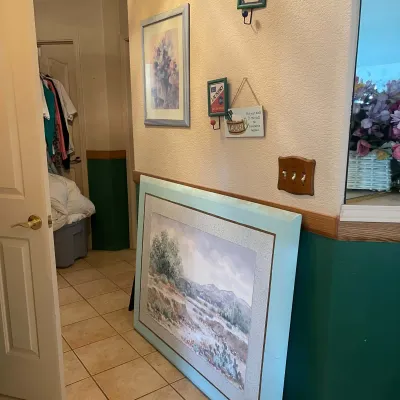 Sale Photo Thumbnail #65: Large framed desert landscape print leaning against a hallway wall, alongside small laundry-themed wall decor and framed artwork.