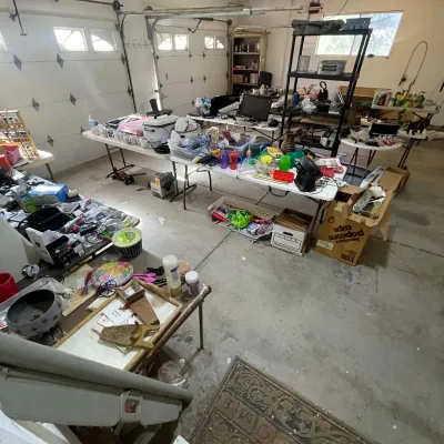 Sale Photo Thumbnail #13: Garage sale setup featuring folding tables and shelving units filled with assorted household goods, kitchenware, electronics, and craft supplies.